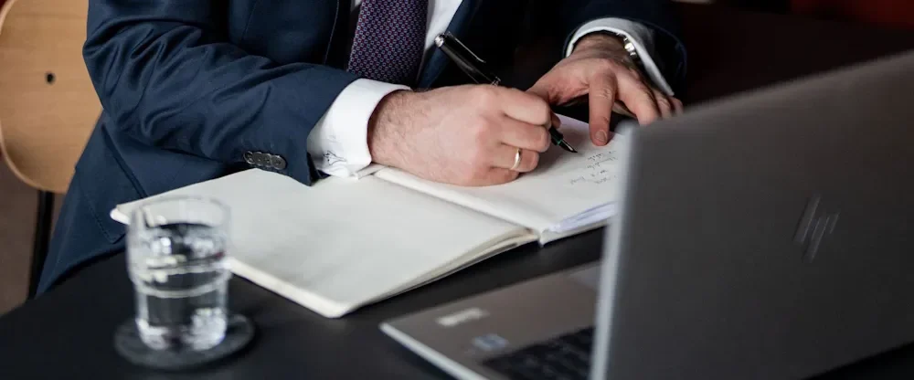 Rechtsanwalt Griemert schreibt in ein Notizbuch, mit einem Laptop und Glas Wasser auf dem Tisch.